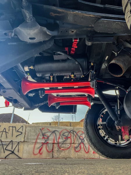 Four red air horns and black tank mounted to frame rails in outdoor install