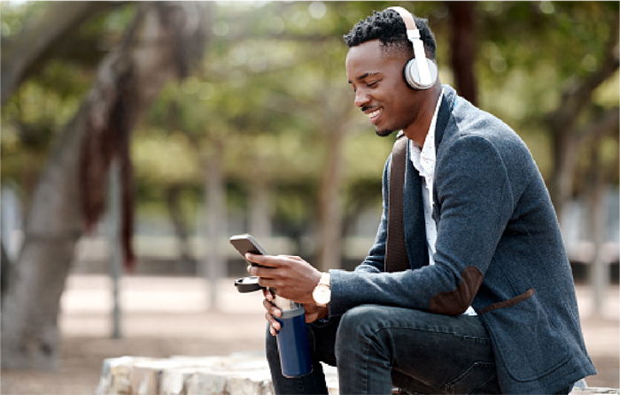 Person wearing headphones, sitting outdoors, looking at a smartphone.