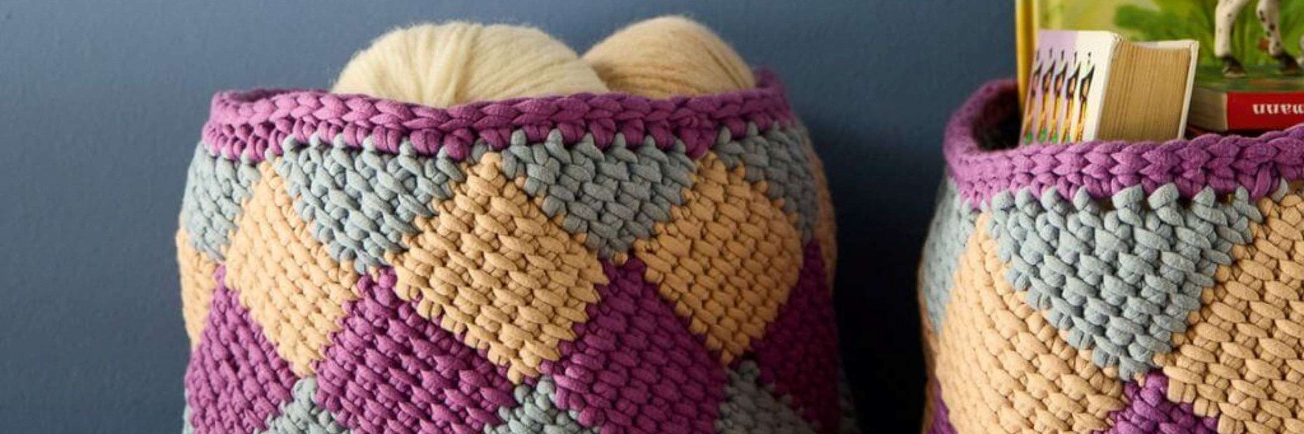 Bunte, tunesisch gehäkelte Körbe mit geometrischen Mustern, gefüllt mit verschiedenen Gegenständen.