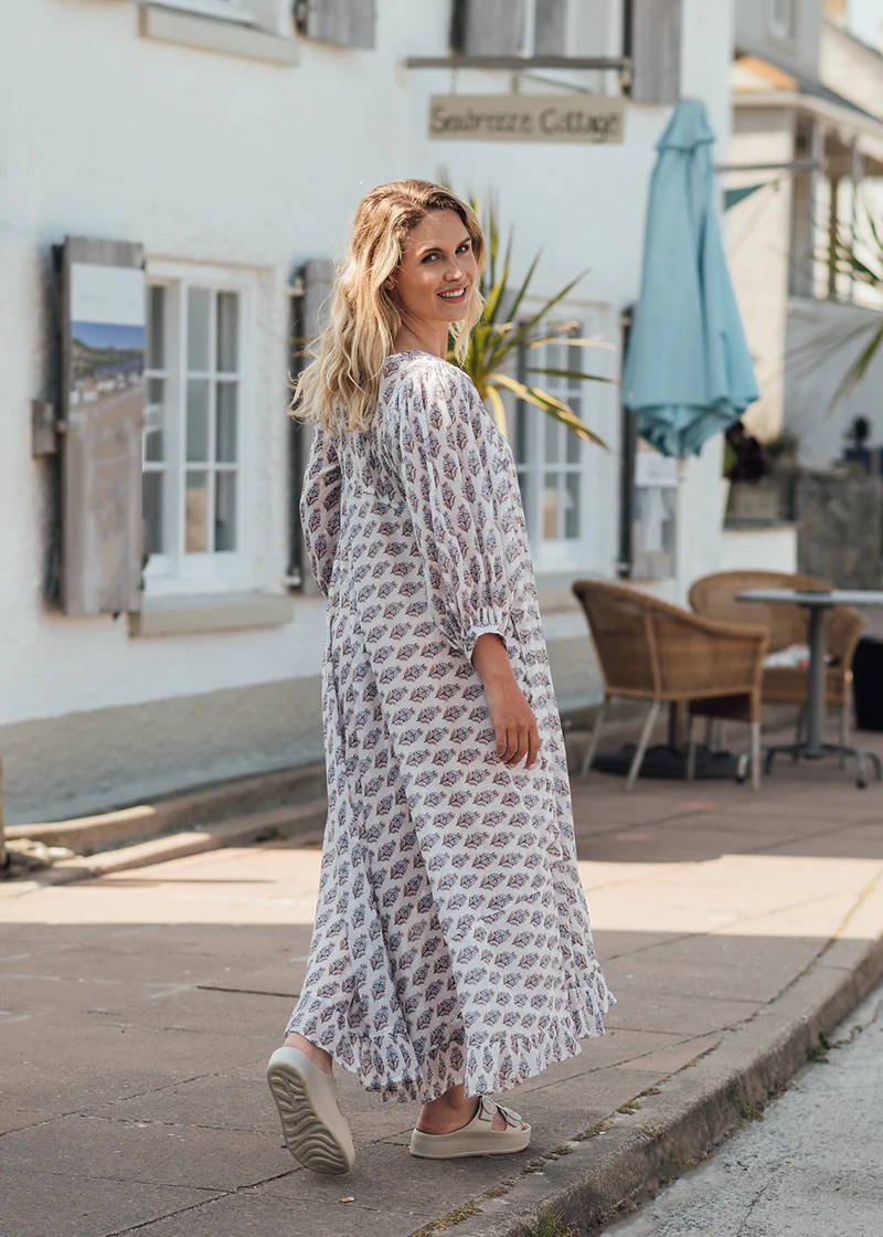 A model wearing an off white paisley printed long floaty dress with long sleeves and off white chunky platform slides