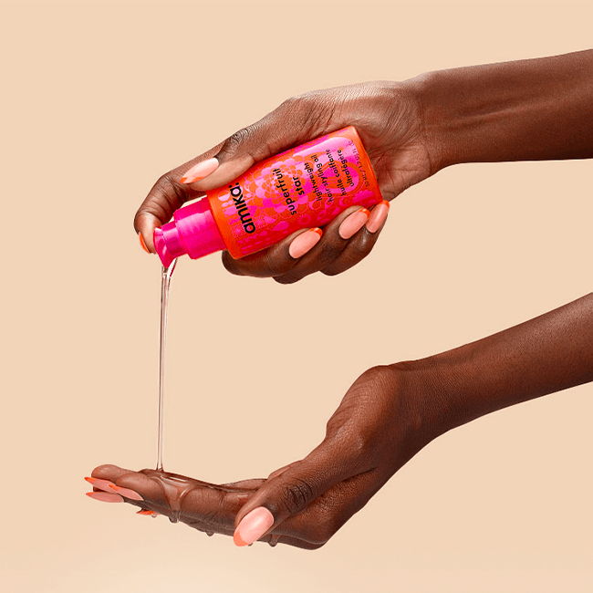 A hand pouring liquid from a pink bottle onto another hand.