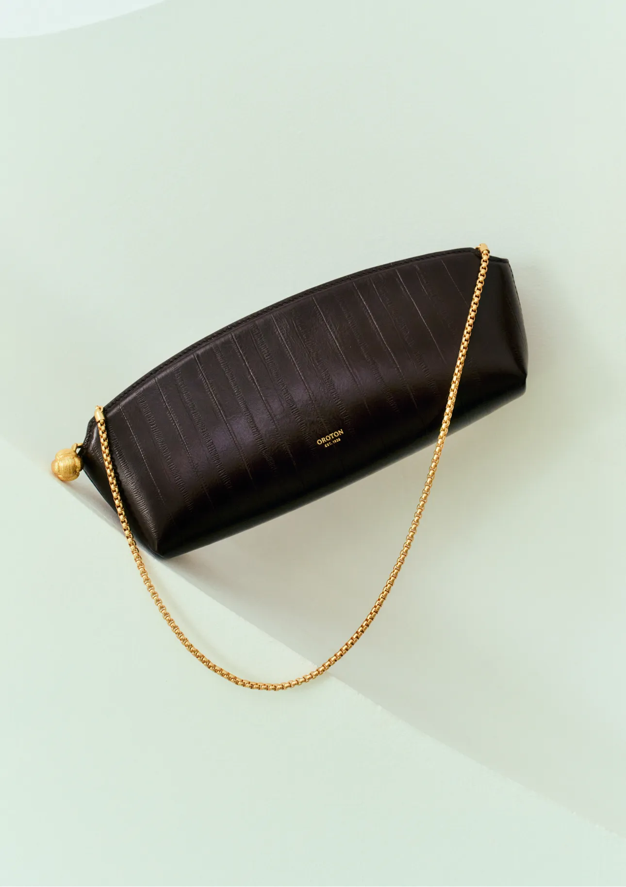 A brown leather clutch with a gold chain on a light background.