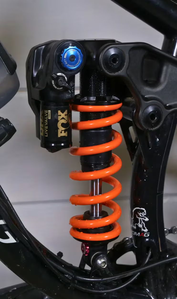 Bicycle shock absorber with orange coil spring and adjustable components.
