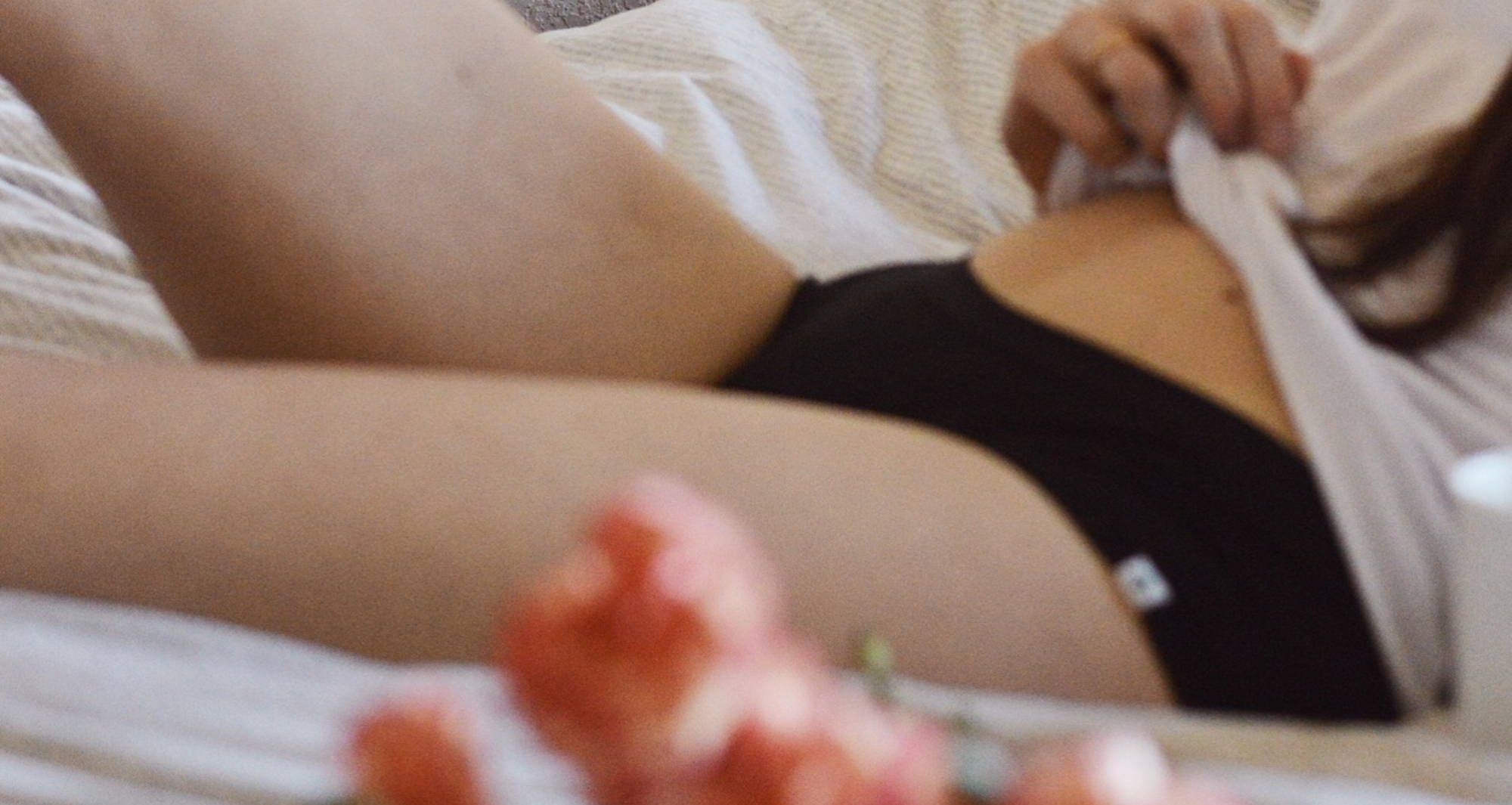 A woman lays on a bed, wearing black underwear and a white tee, with roses in the forefront.