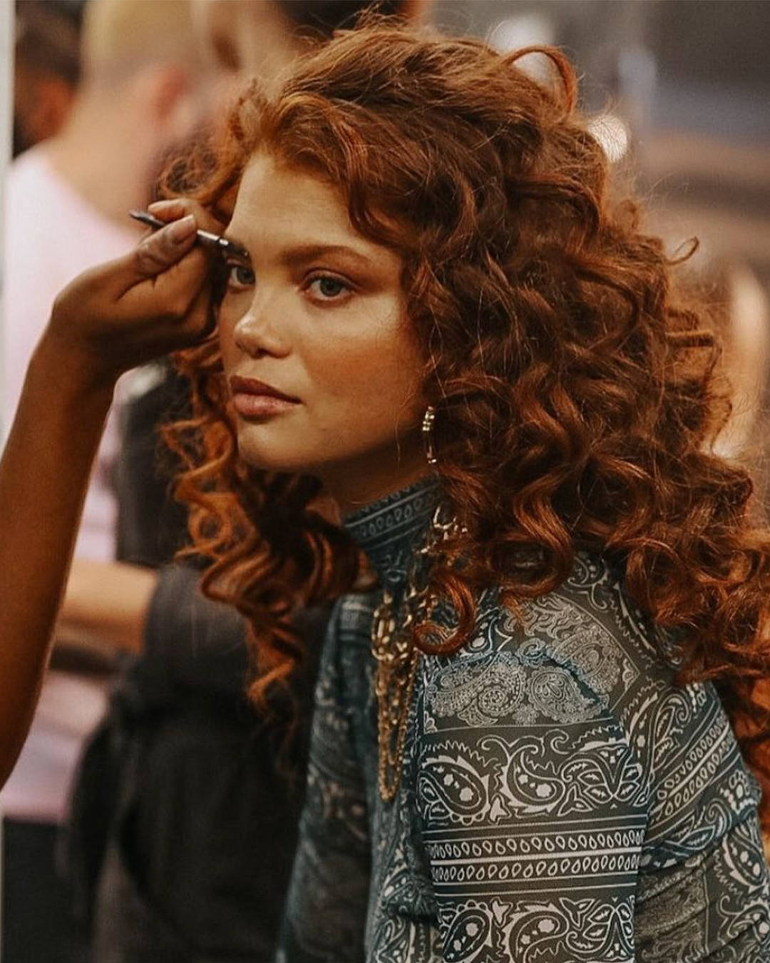 Image of Model at NYFW with voluminous red curls getting her eyebrow makeup done