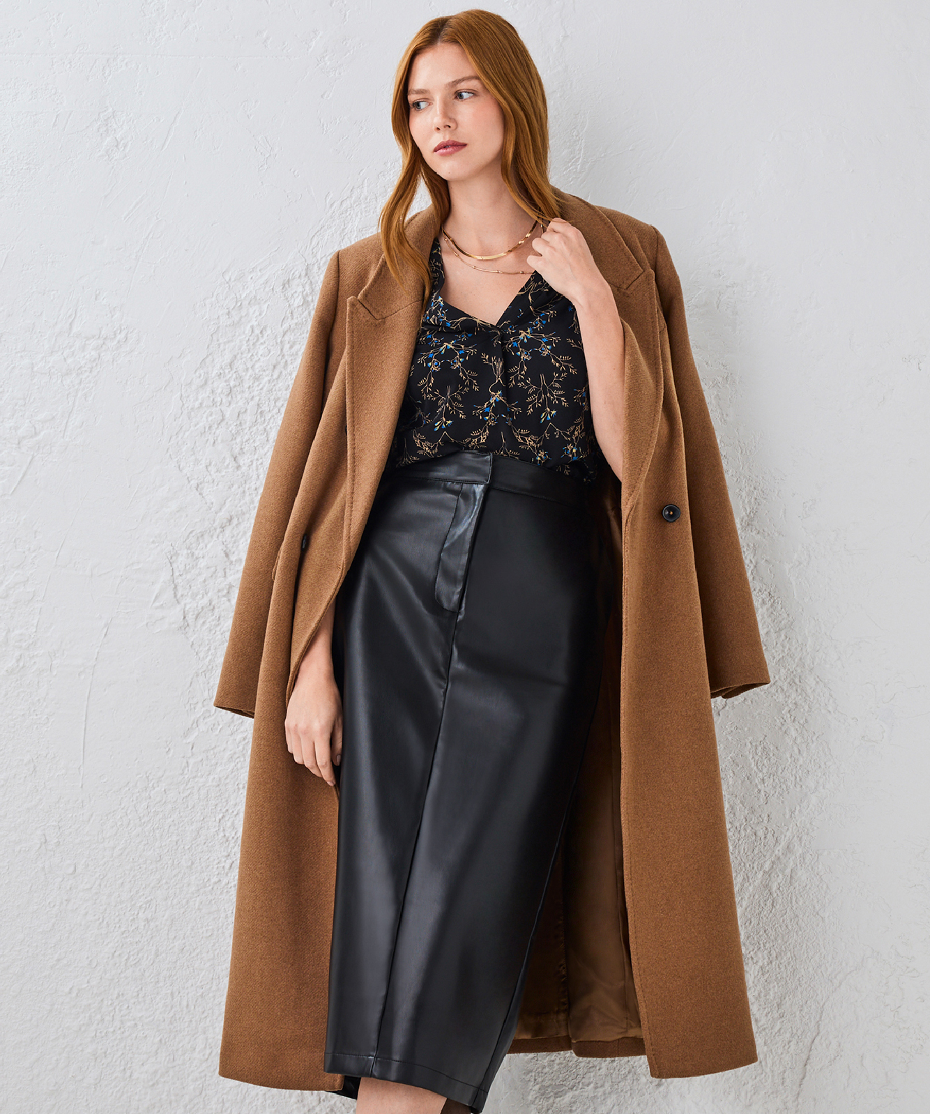 Woman in a brown coat and black skirt against a light background.