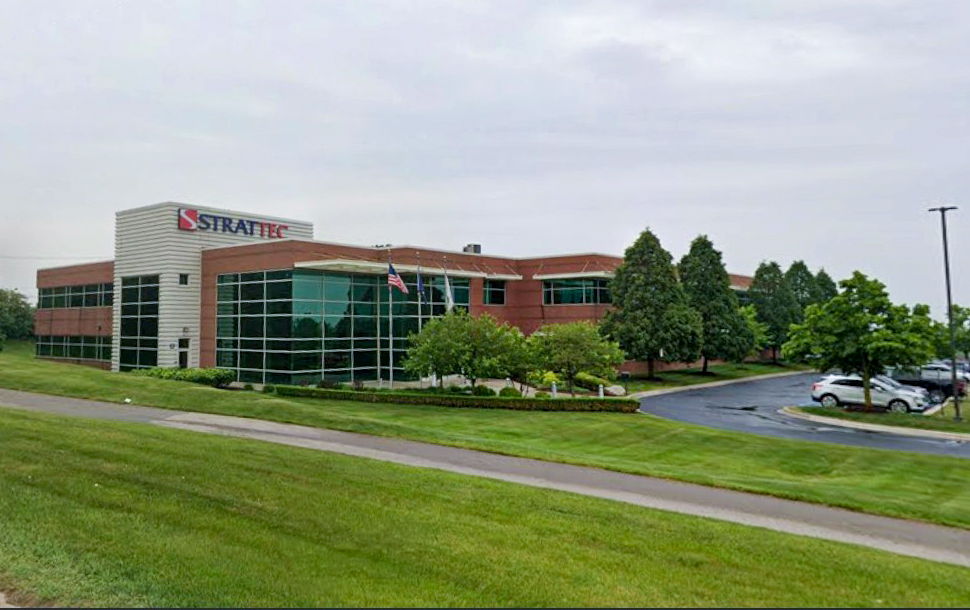 Modern office building surrounded by grass and trees under a cloudy sky.