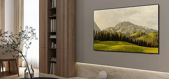 An OLED TV showing a mountain landscape in a modern living room setting.