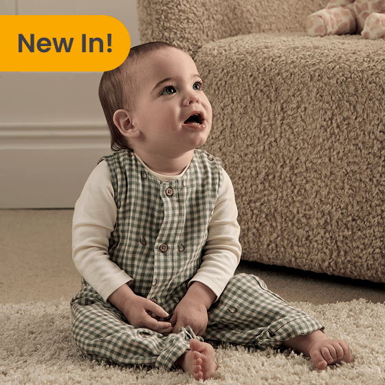 Baby sitting on a carpet, wearing a checkered outfit, looking up.