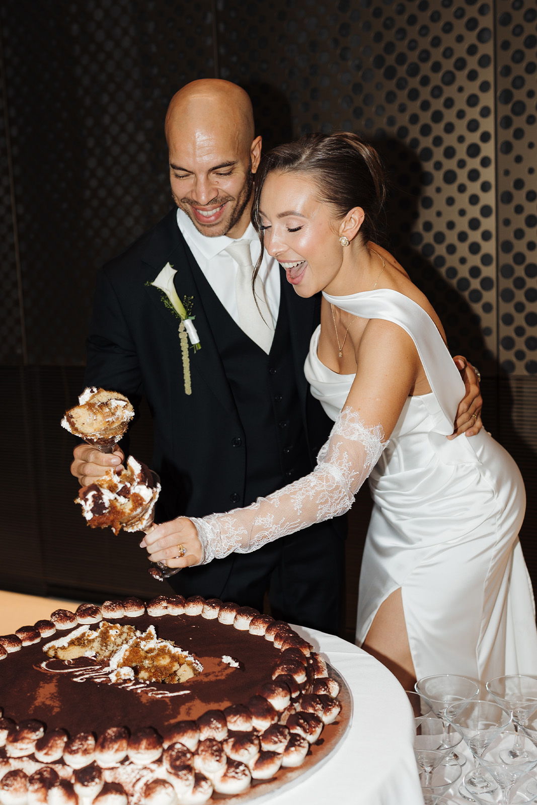 Bride and groom joyfully serve cake at their wedding reception.