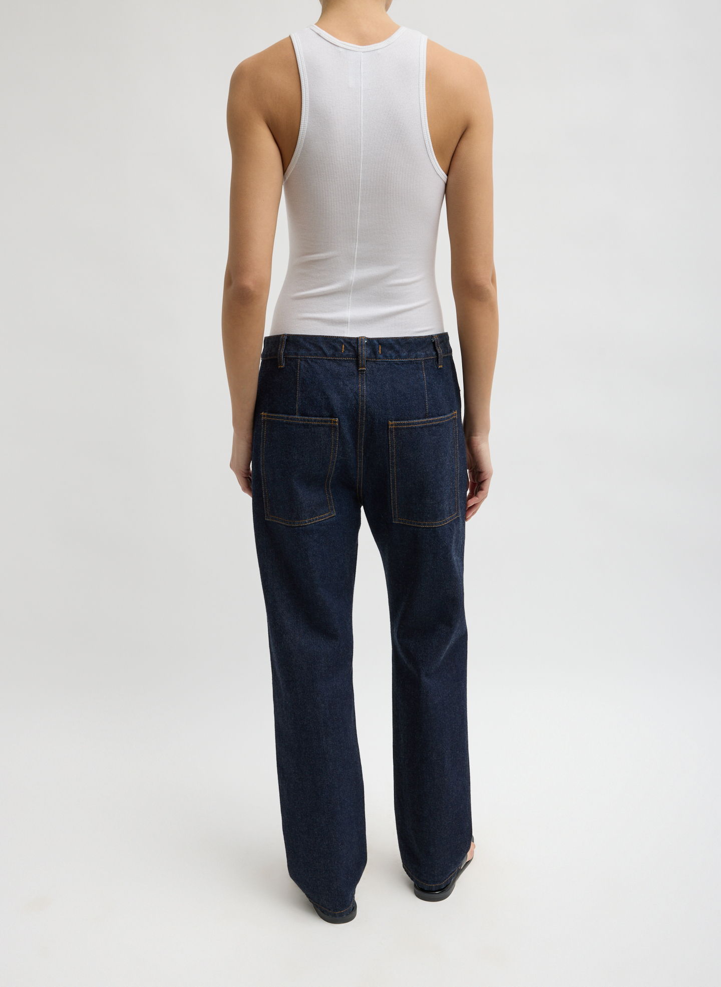 Person wearing a white tank top and blue jeans, viewed from the back.