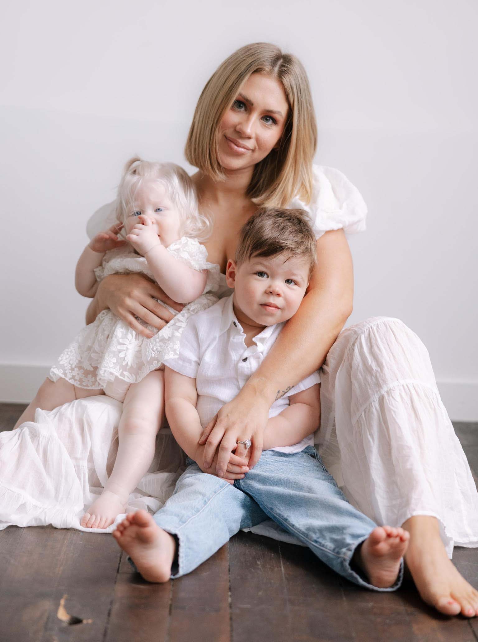 Woman sitting on the floor with two children, smiling together in a cozy setting.