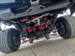 Low-angle view of four red train horns with wheel ring lights mounted above rear axle on lifted truck