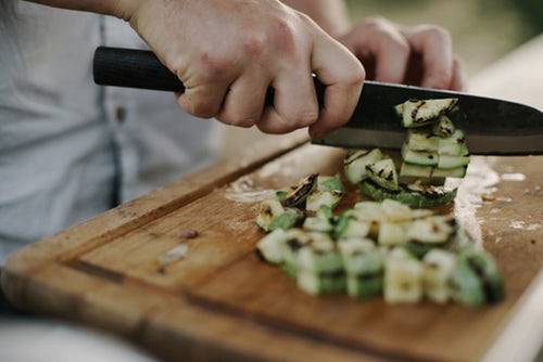 hands holding a knife and cutting vegetables on the best cutting board for sushi