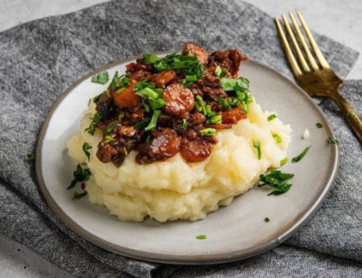 Plate of mashed potatoes topped with meat and herbs, garnished with parsley.