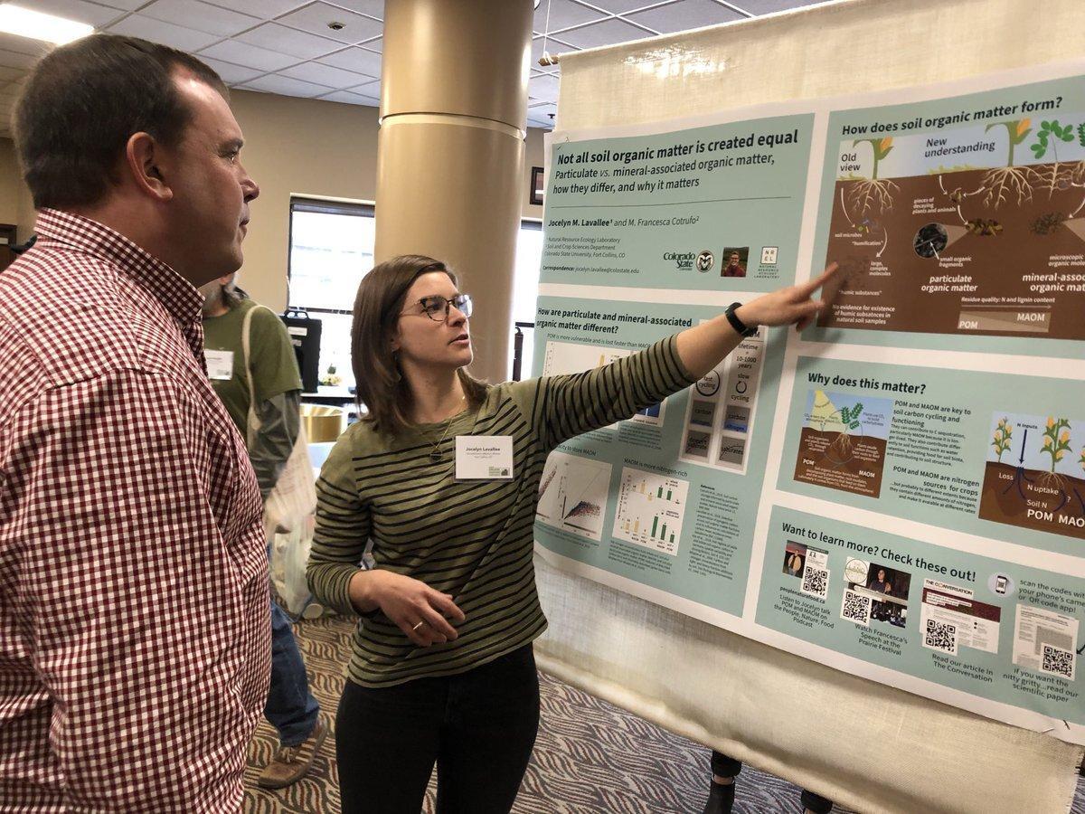 A woman explains a poster to a man in an indoor setting.