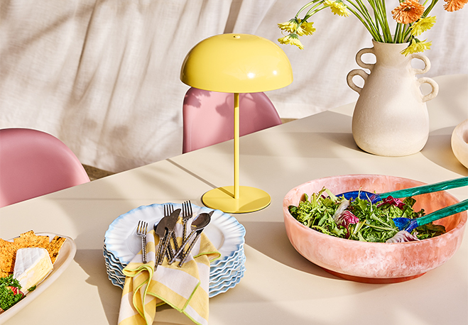 Table set with colorful bowls, utensils, a lamp, and fresh flowers.