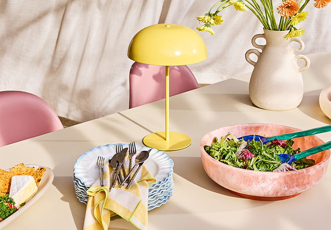 Table set with colorful bowls, utensils, a lamp, and fresh flowers.