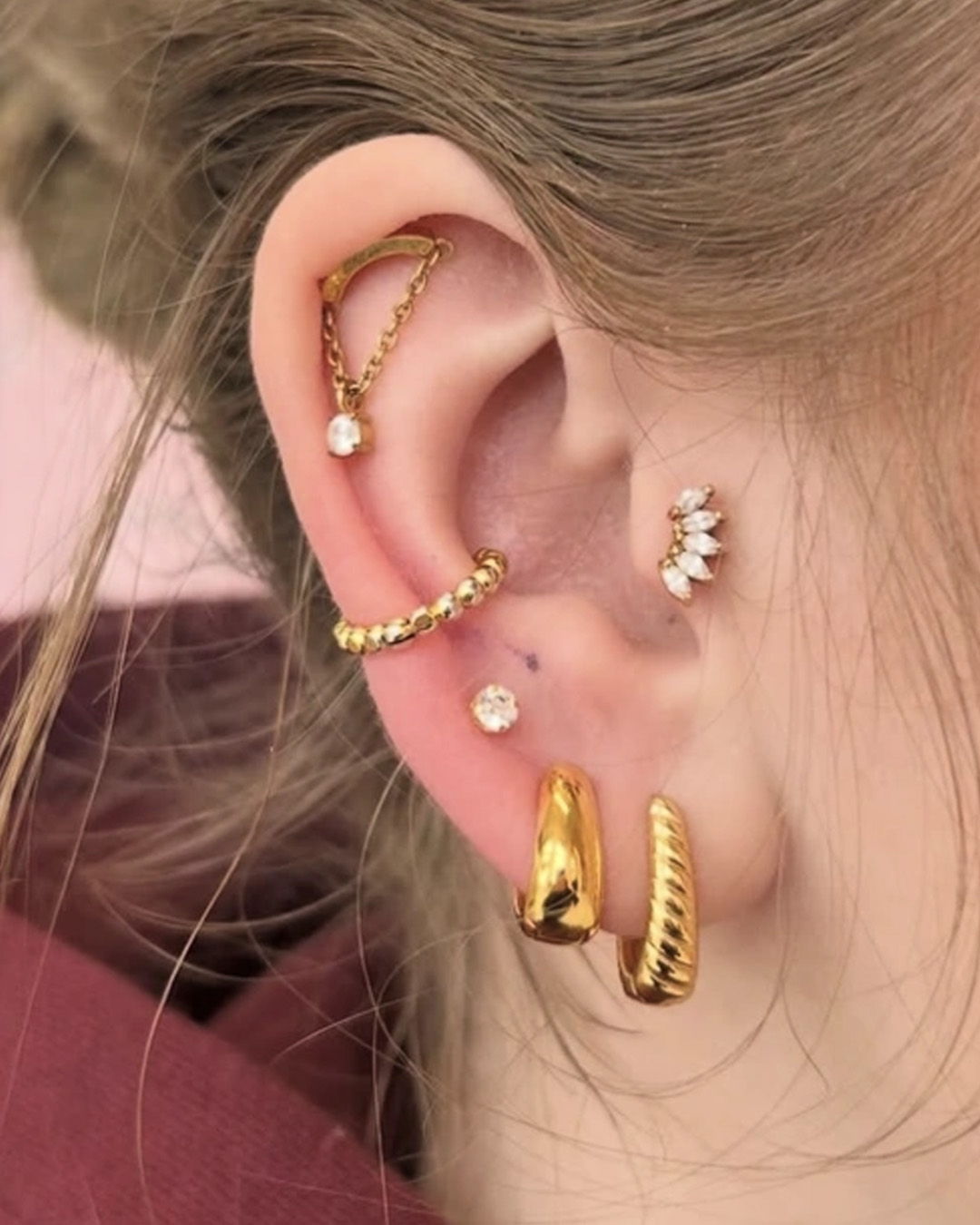 Close-up of an ear adorned with multiple gold and silver earrings.