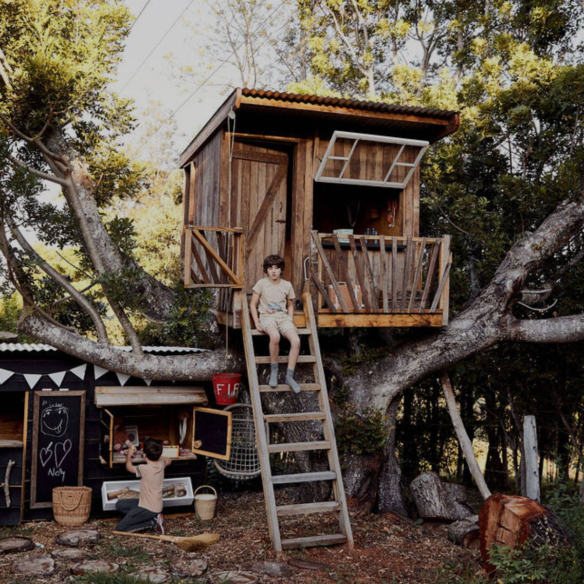 A boy sitting on the ladder to the treehouse, raised cubby house