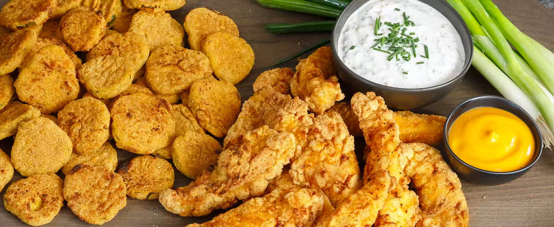 Arrangement of air-fried pickles and chicken tenders, with bowls of dipping sauces and green onions