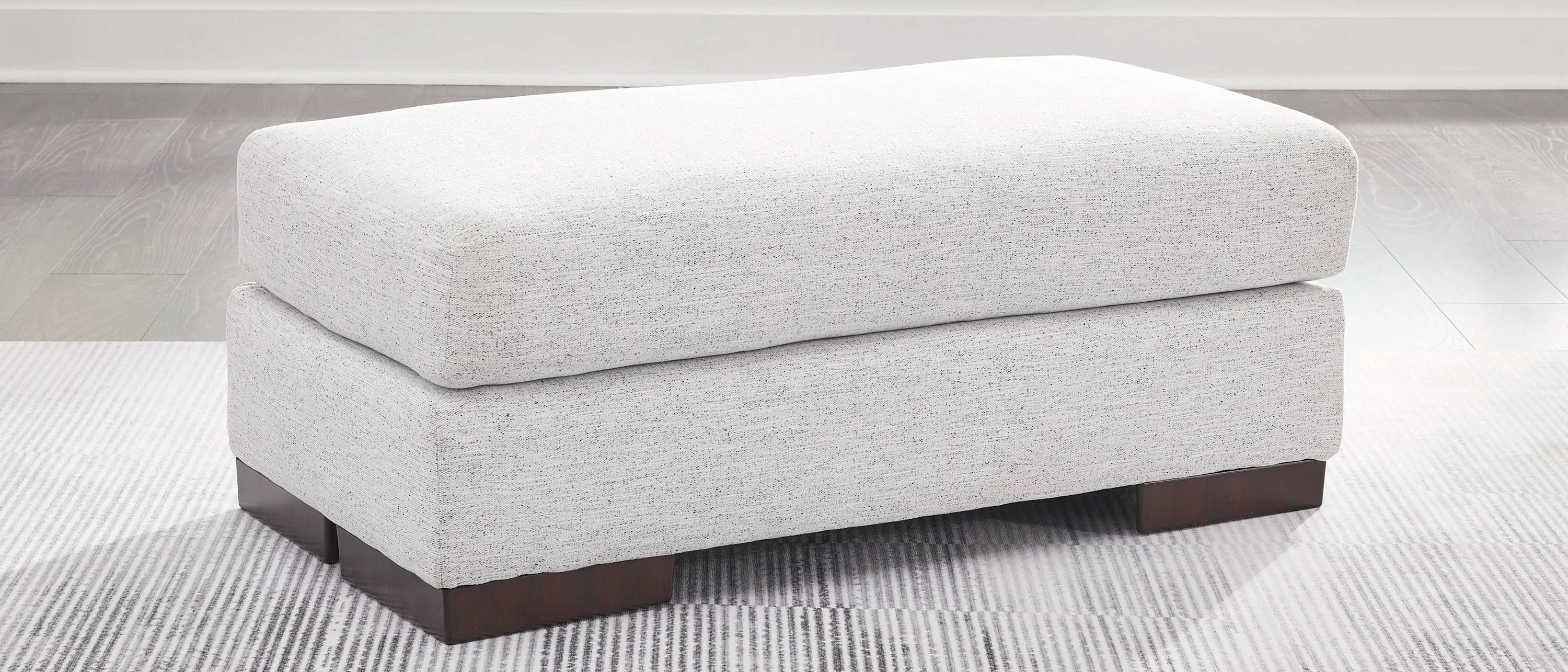White upholstered ottoman with wooden legs in a bright room.