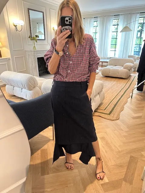 Woman in a checkered shirt and skirt taking a mirror selfie indoors.