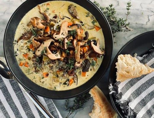Bowl of creamy soup with mushrooms, herbs, and bread on a table.