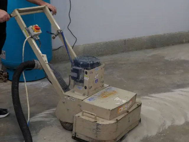 Using concrete and hand grinders to scratch the concrete slab, ensuring a clean surface for the application of the moisture seal epoxy primer.