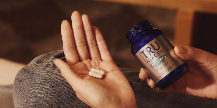 Person holding a supplement capsule and a blue bottle of vitamins.