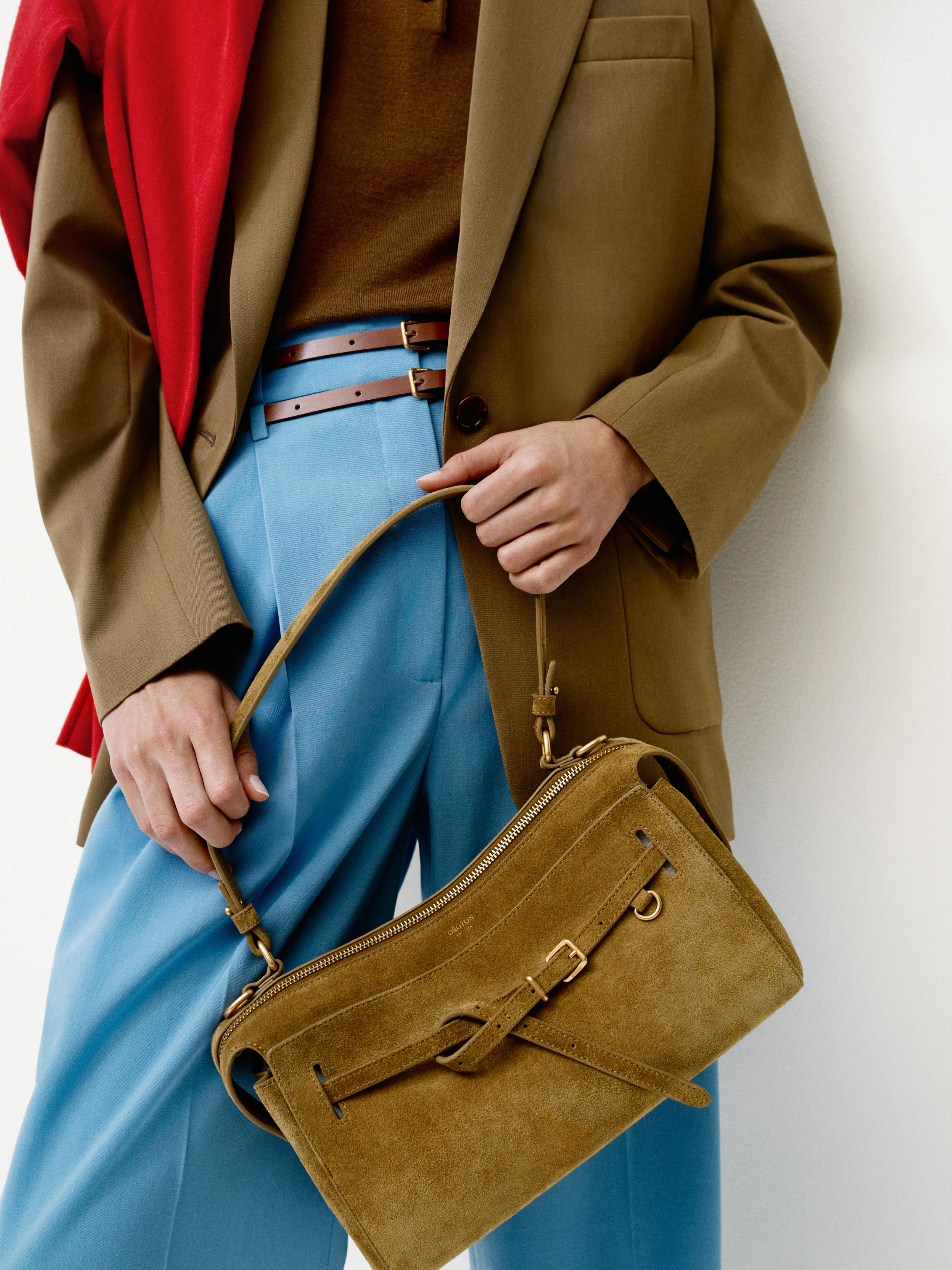 Person holding a brown handbag, wearing a brown blazer and blue trousers.
