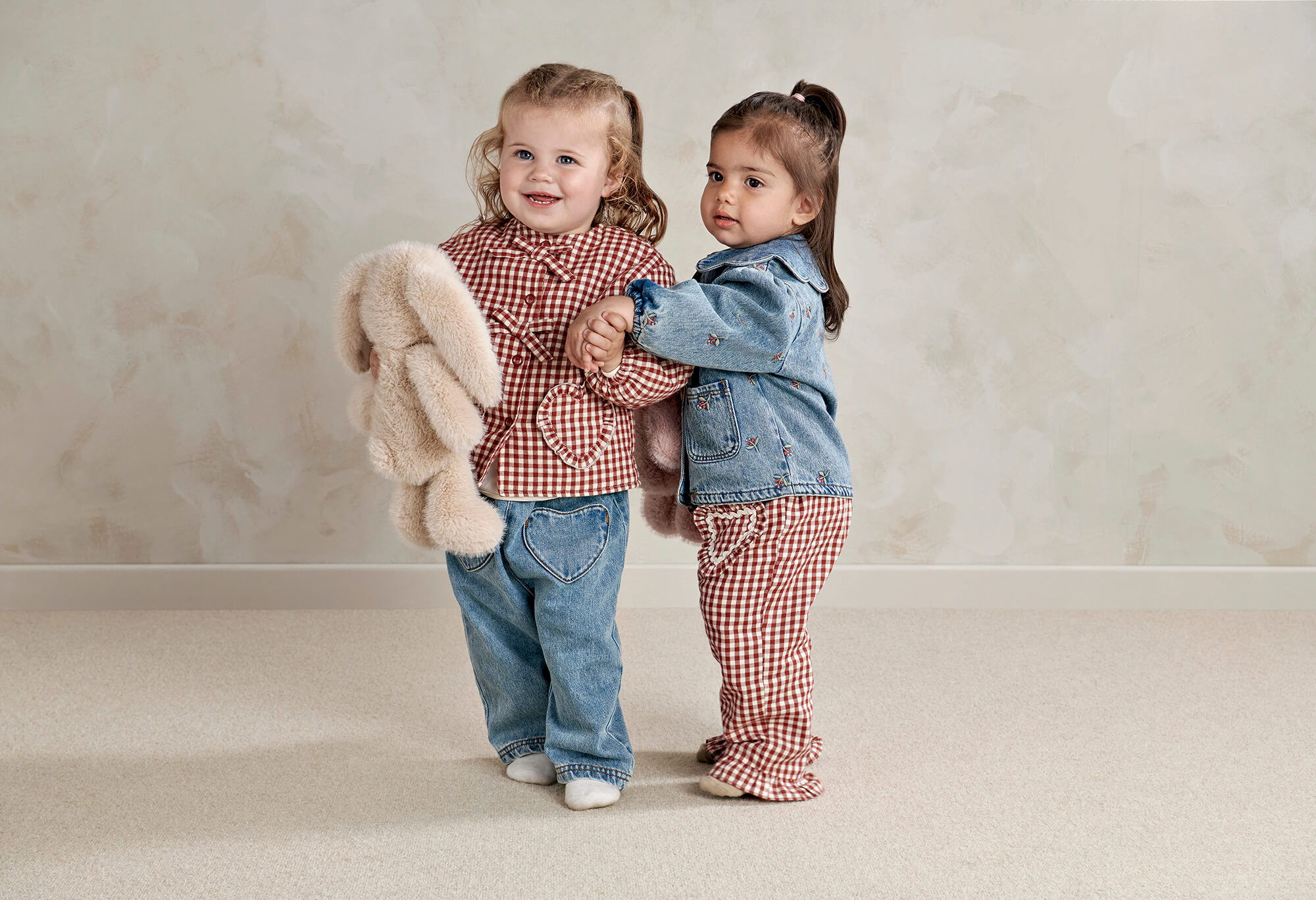 Two young girls smiling, one holding a stuffed animal, in casual outfits.
