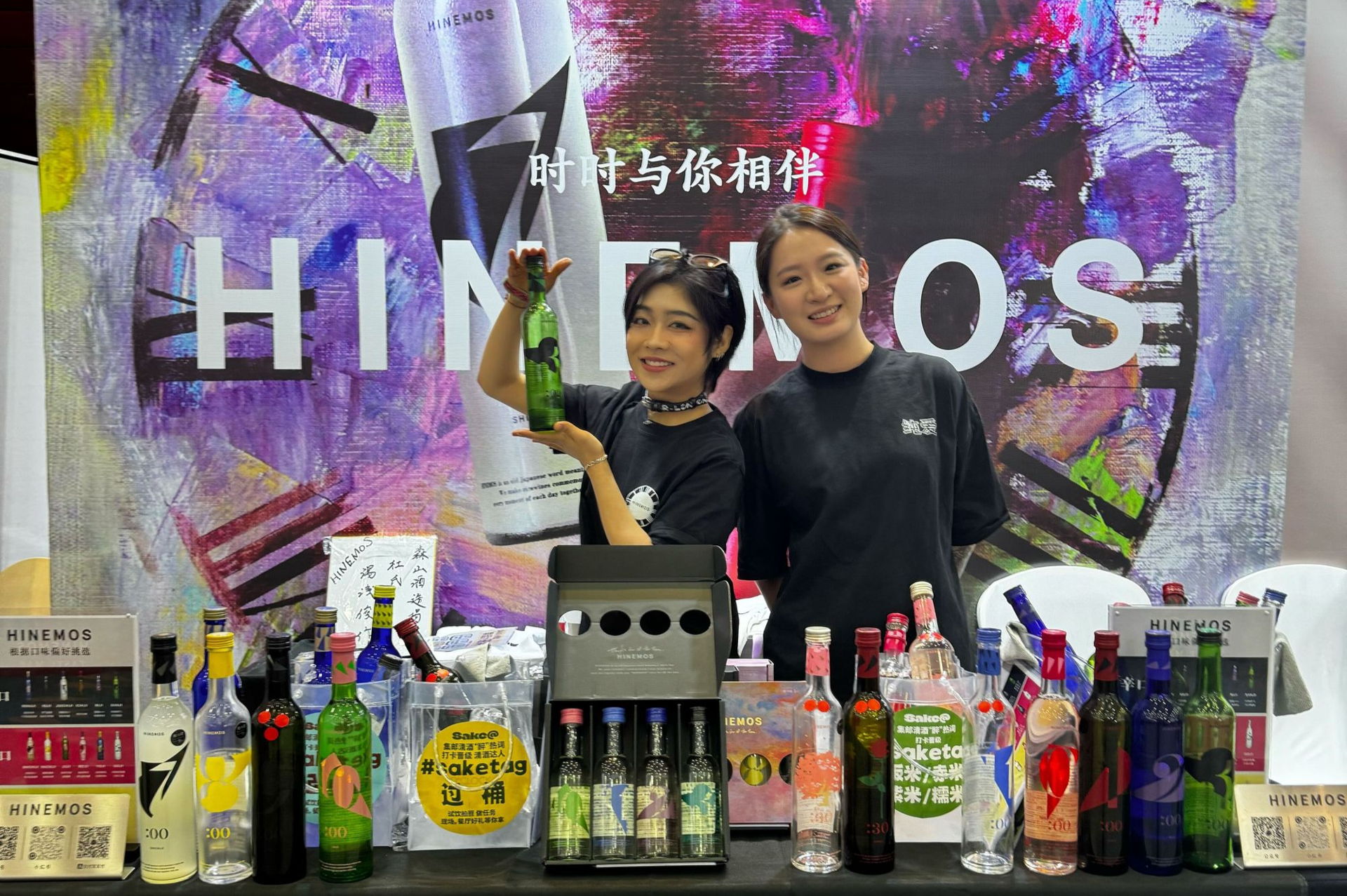 Two bartenders with various bottles at a colorful bar display.