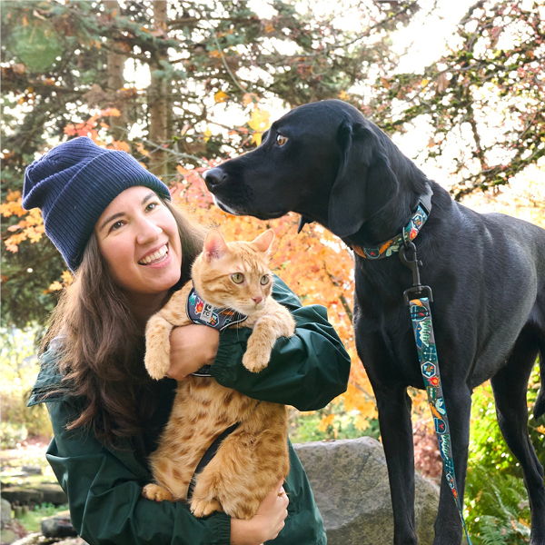 A woman holds a cat while a dog stands beside her.