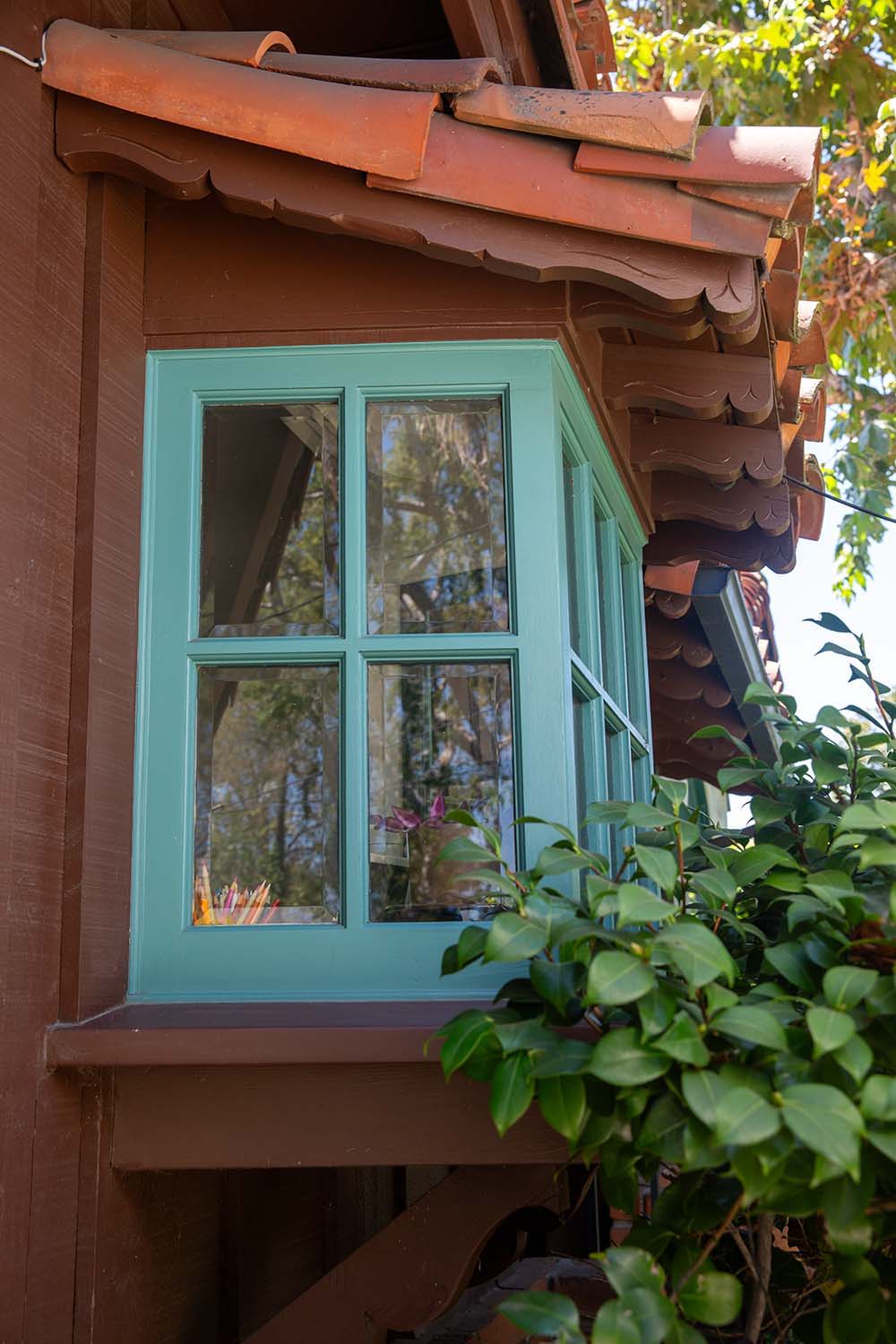 A kitchen window addition on a vintage home with hand carved rafter tails above it. The window is painted teal.