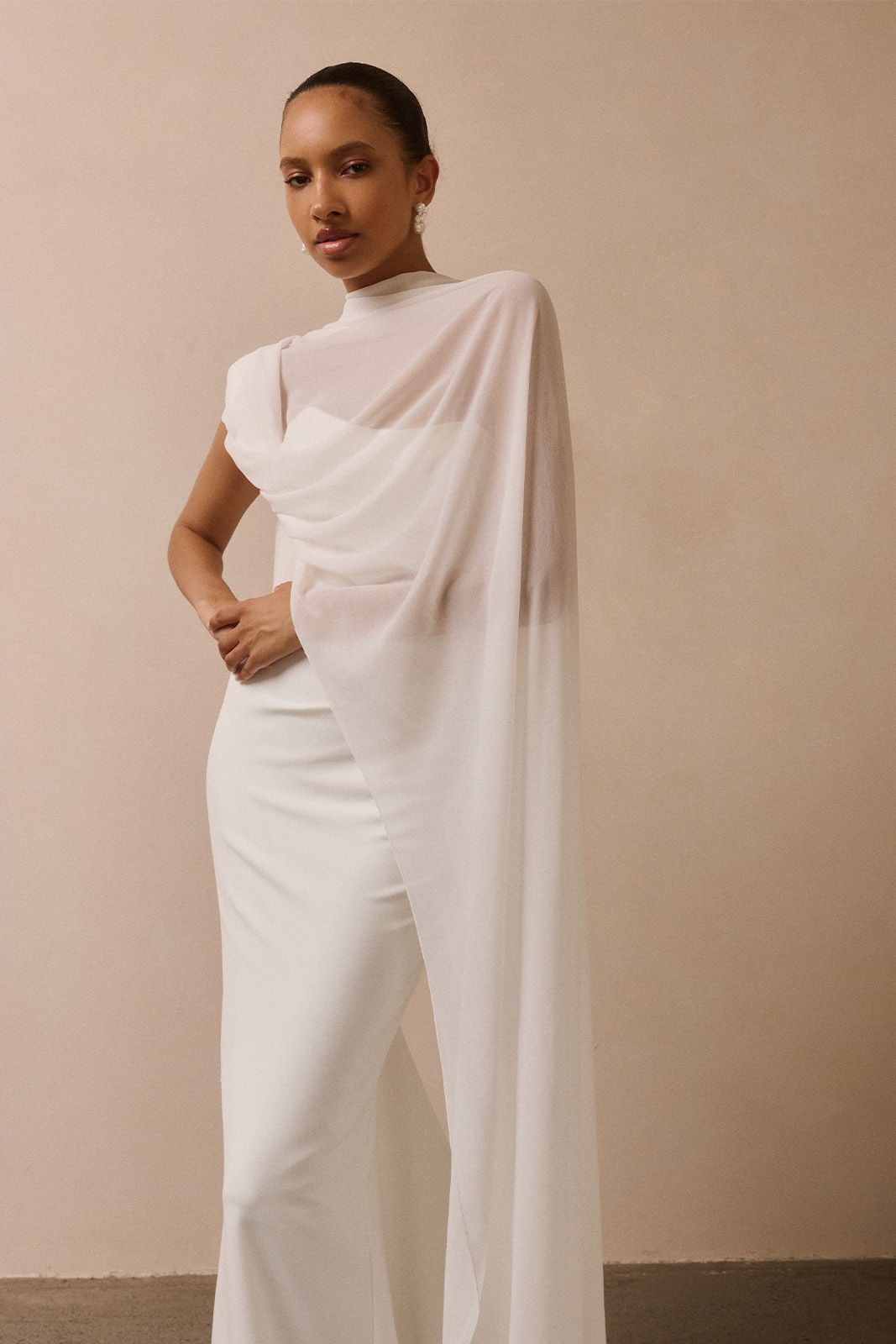 Model in a stylish white outfit with a flowing cape.