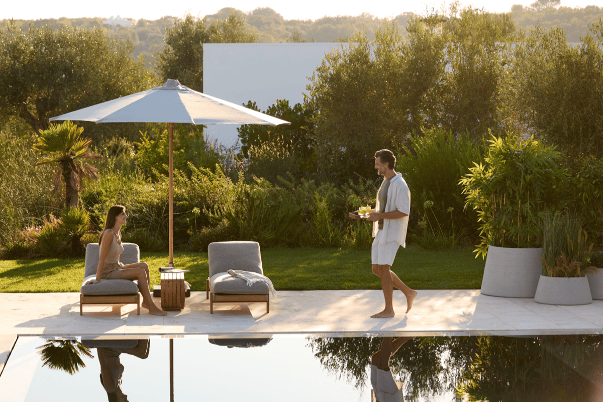 Poolside loungers with a large patio umbrella at golden hour, set beside a modern pool with lush garden planting in the background.