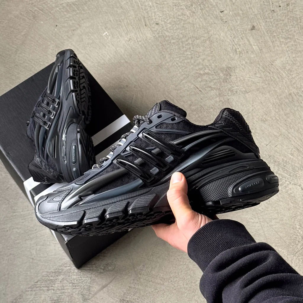 A hand holding a pair of black athletic shoes beside a box.