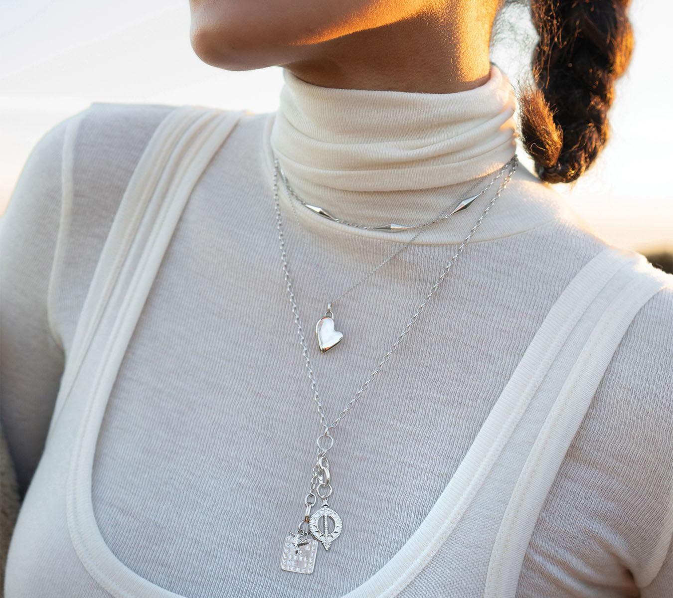 A close-up of a person wearing layered silver necklaces.