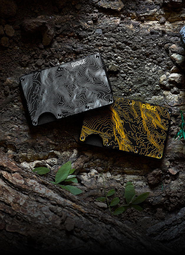Two stylish wallets on a textured surface with greenery.