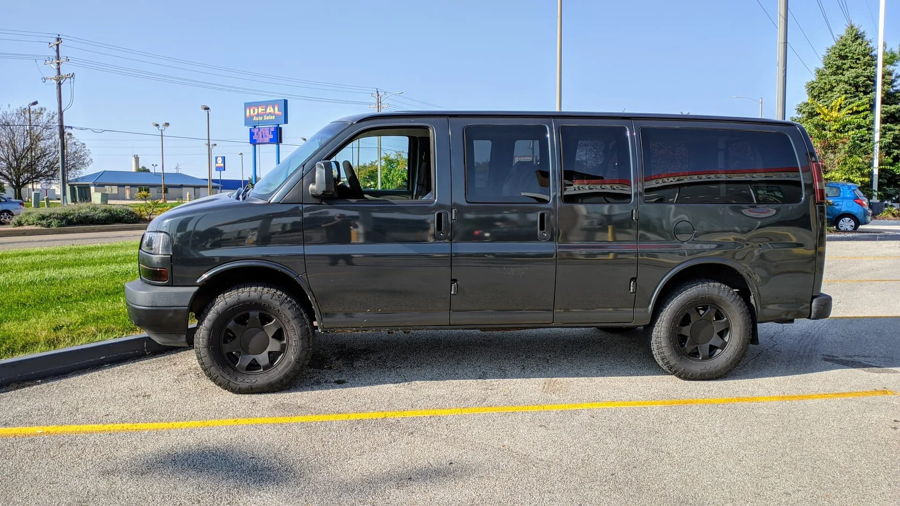 Side profile dark gray GMC Savana AWD matte black wheels Nitto all-terrain tires Ideal Auto Sales parking lot Pat's Conductor's Special 127H featured gallery photo 1
