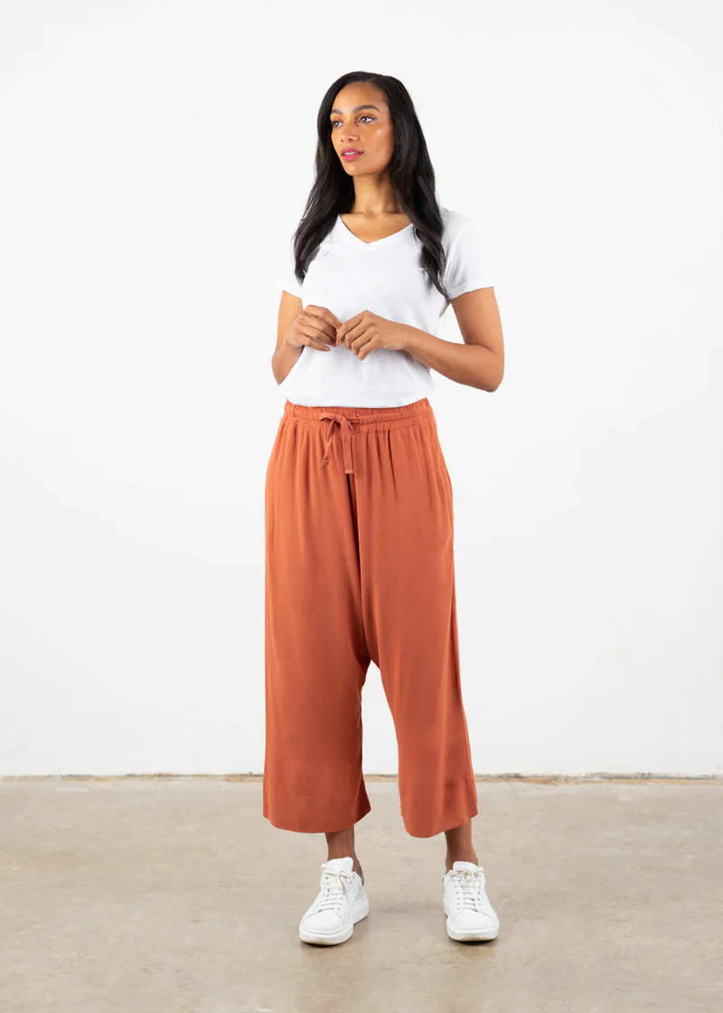 A model wearing a white top with orange, loose fitting drop crotch trousers and white trainers