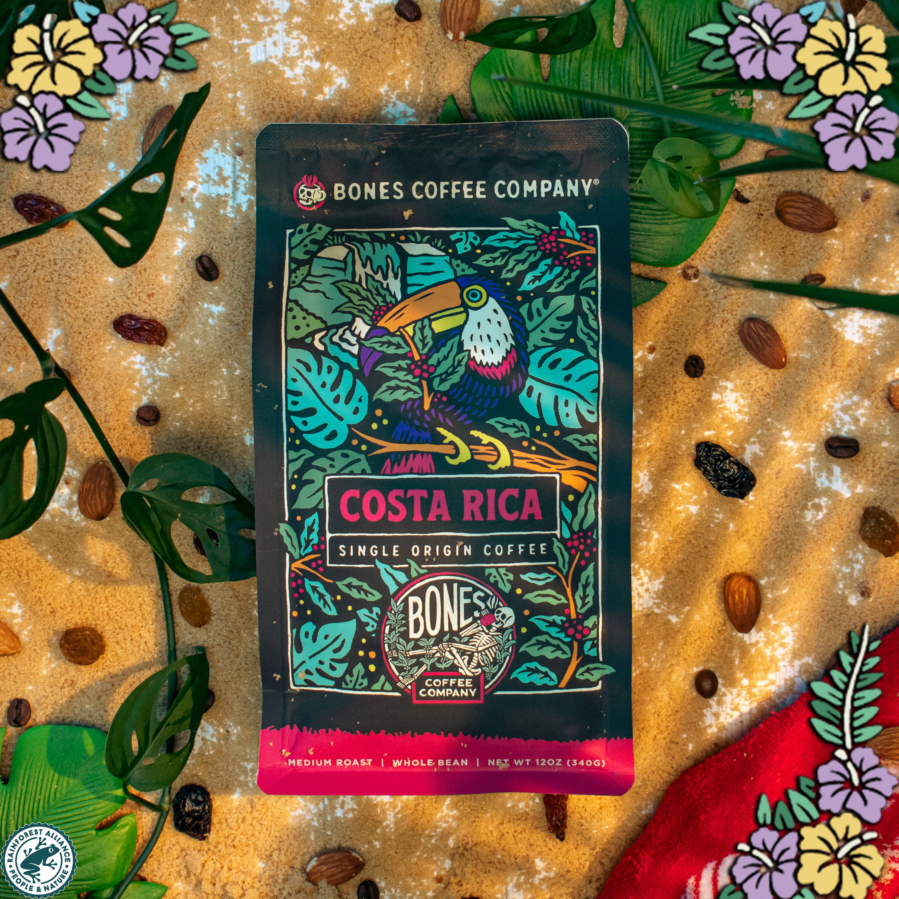 A 12 ounce bag of coffee from Costa Rica that has art of a toucan on it. There are flowers in the top left, top right, and bottom right. There's also the logo for the Rainforest Alliance in the bottom left.