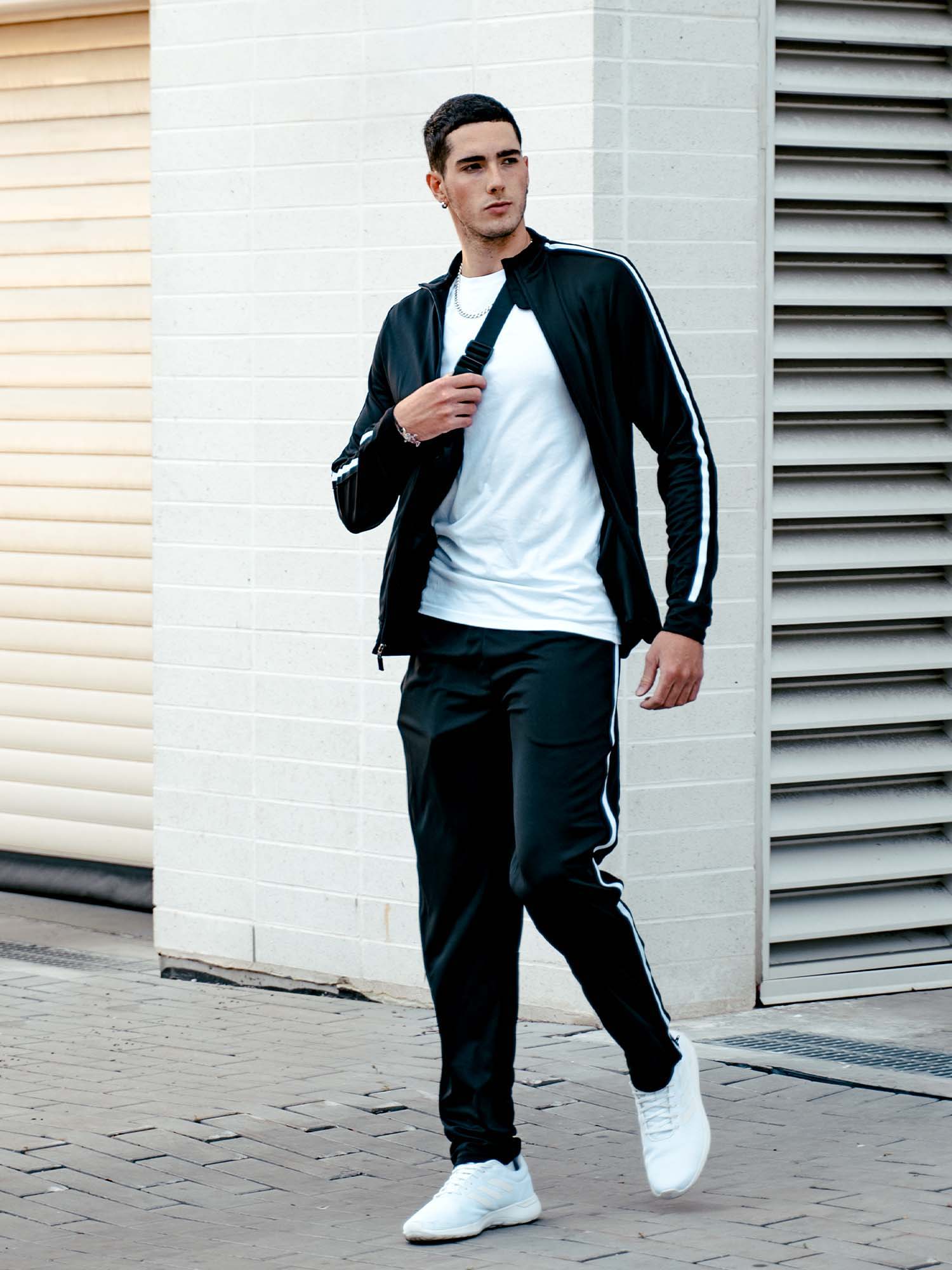 Tall man walking outside wearing a black athletic jacket and pants with a white stripe down the side.