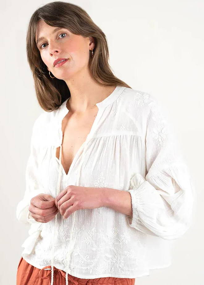 A model wearing a white floaty bohemian long sleeved blouse with balloon sleeves, fitted cuffs and embroidery details.