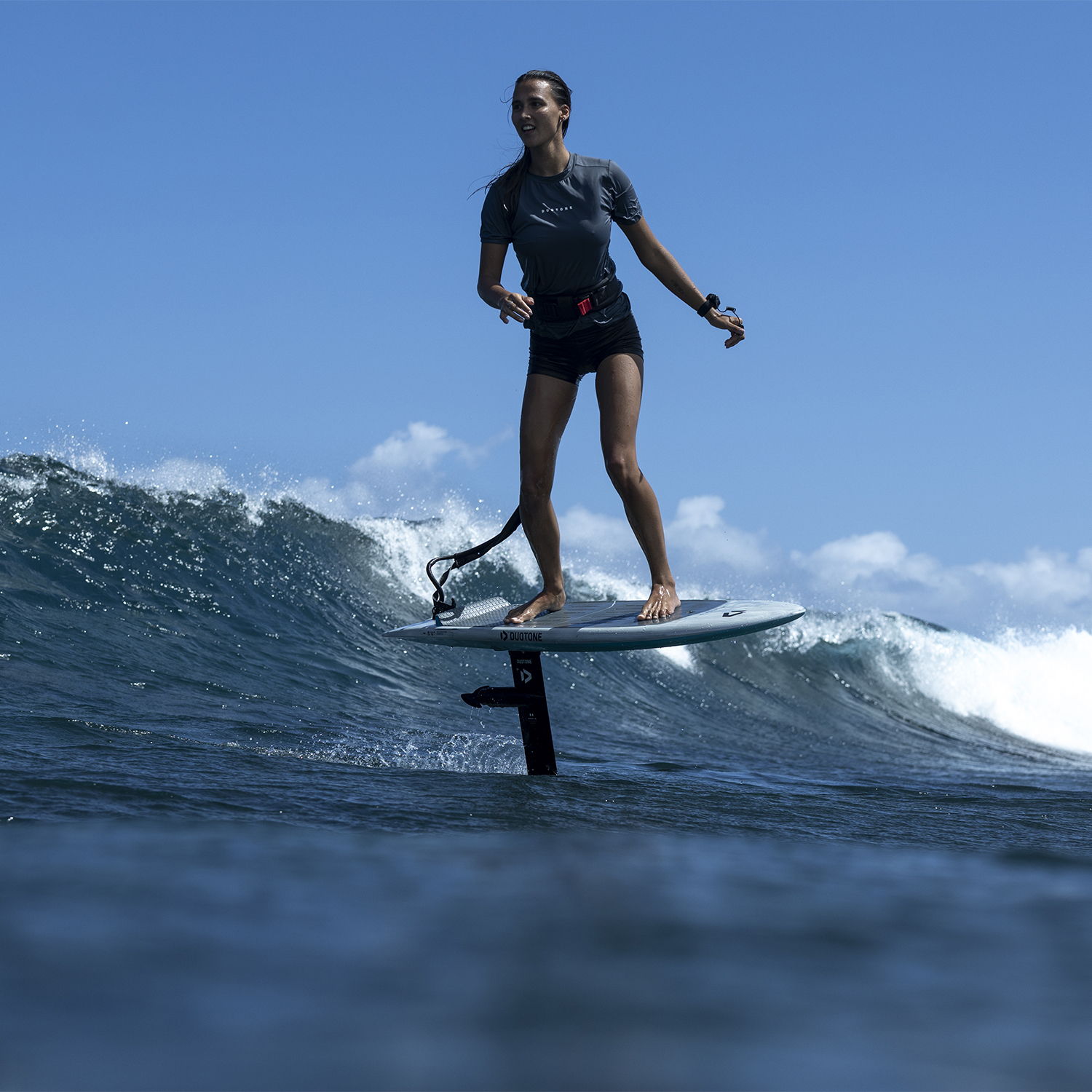 Une personne faisant du surf sur un Duotone Foil Assist, E-foil dans l'océan, sous un ciel bleu limpide.