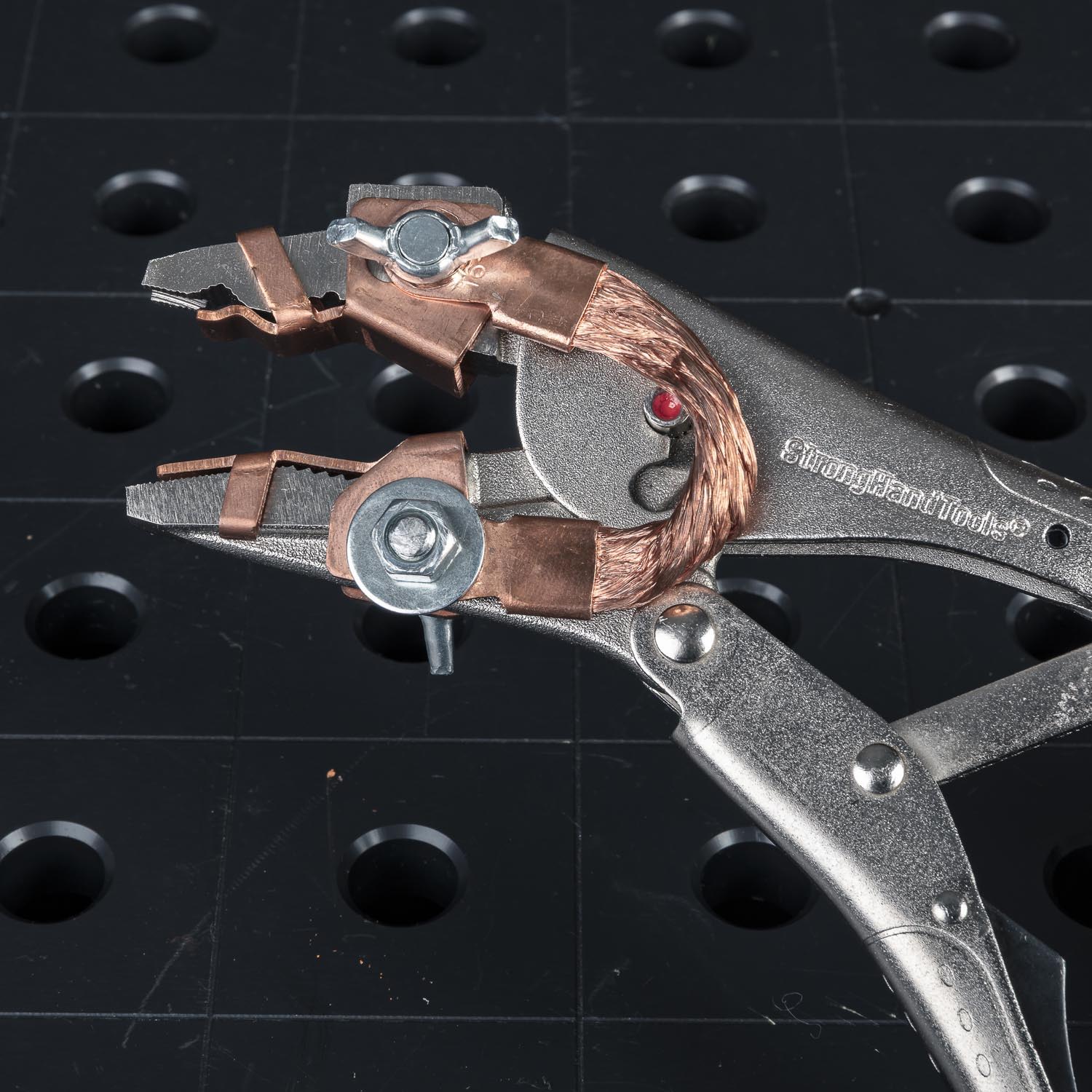 A close-up of a metal locking pliers on a black perforated surface.