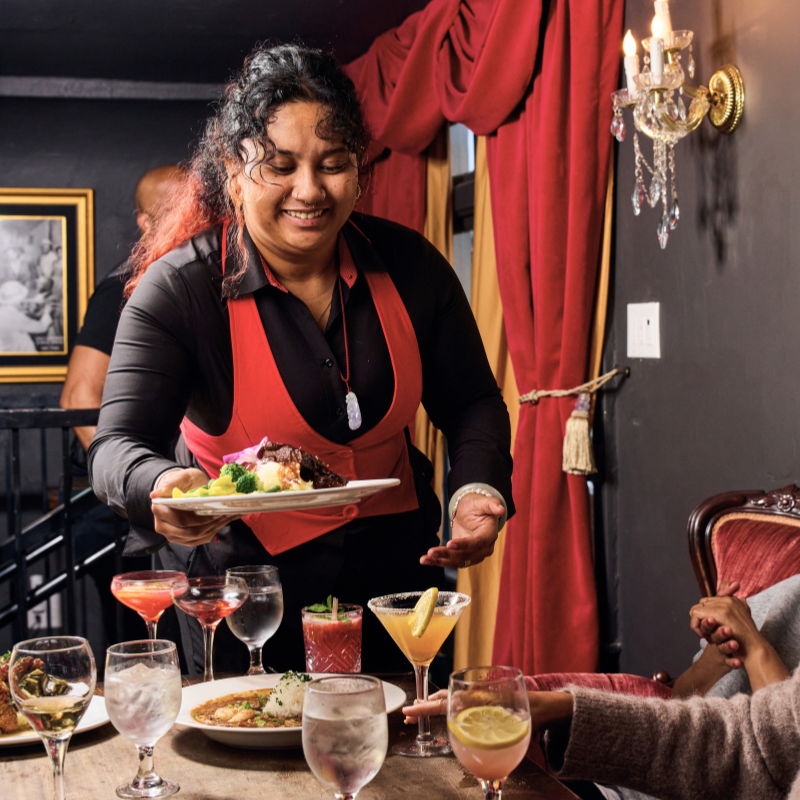 Waitress serving food and drinks at a restaurant table.