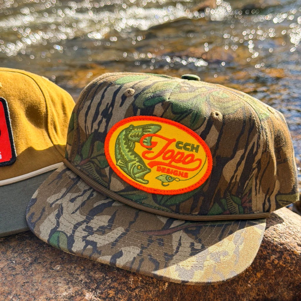 Two caps resting by a river, one with a fish logo.