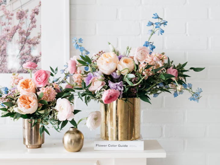 Vases with colorful flowers on a white mantelpiece against a light wall.
